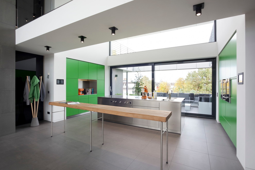 Photo of a large contemporary open plan kitchen in Cologne with a double-bowl sink, flat-panel cabinets, green cabinets, stainless steel benchtops, with island, white splashback, coloured appliances and concrete floors.