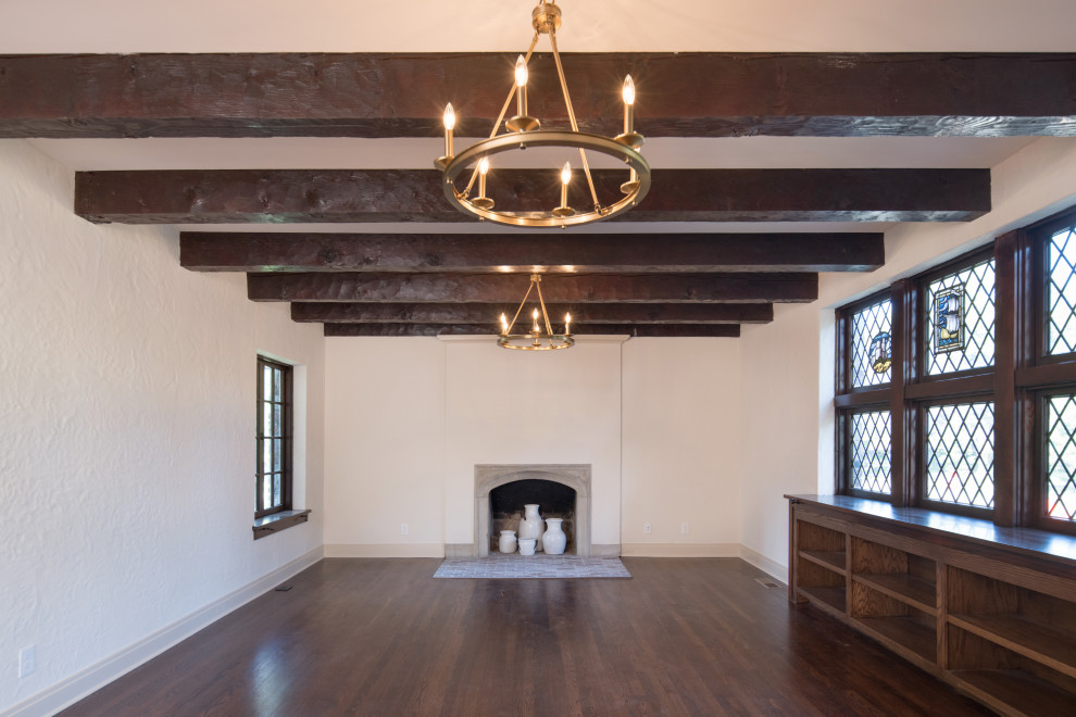 This is an example of a large traditional enclosed living room in Kansas City with a library, white walls, dark hardwood floors, a standard fireplace, a concrete fireplace surround, no tv, brown floor and exposed beam.