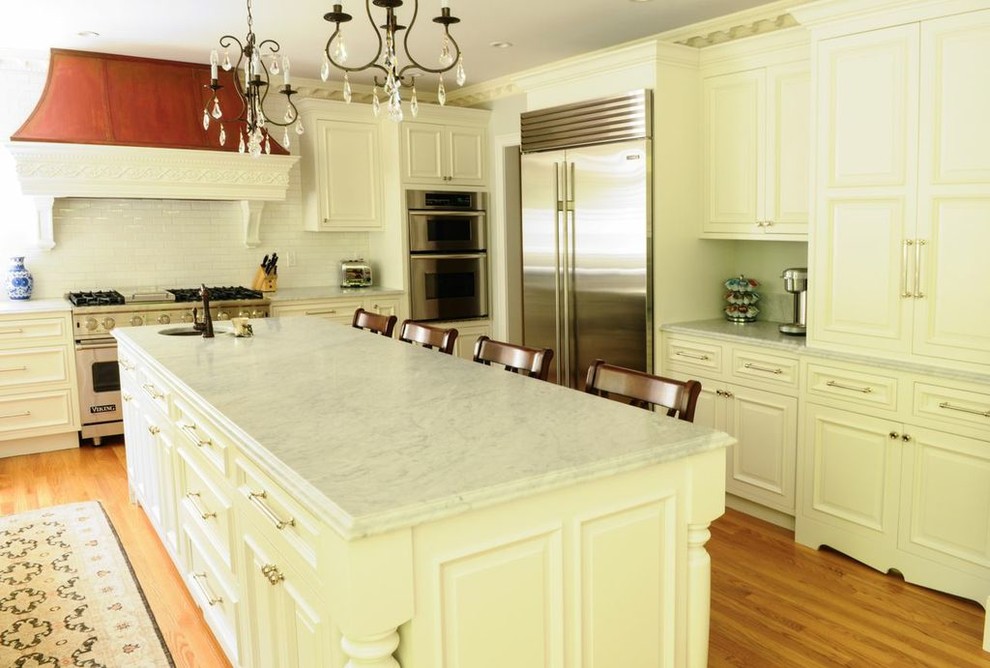 Photo of a large traditional eat-in kitchen in Boston with a farmhouse sink, raised-panel cabinets, white cabinets, marble benchtops, subway tile splashback, stainless steel appliances, white splashback, light hardwood floors and with island.