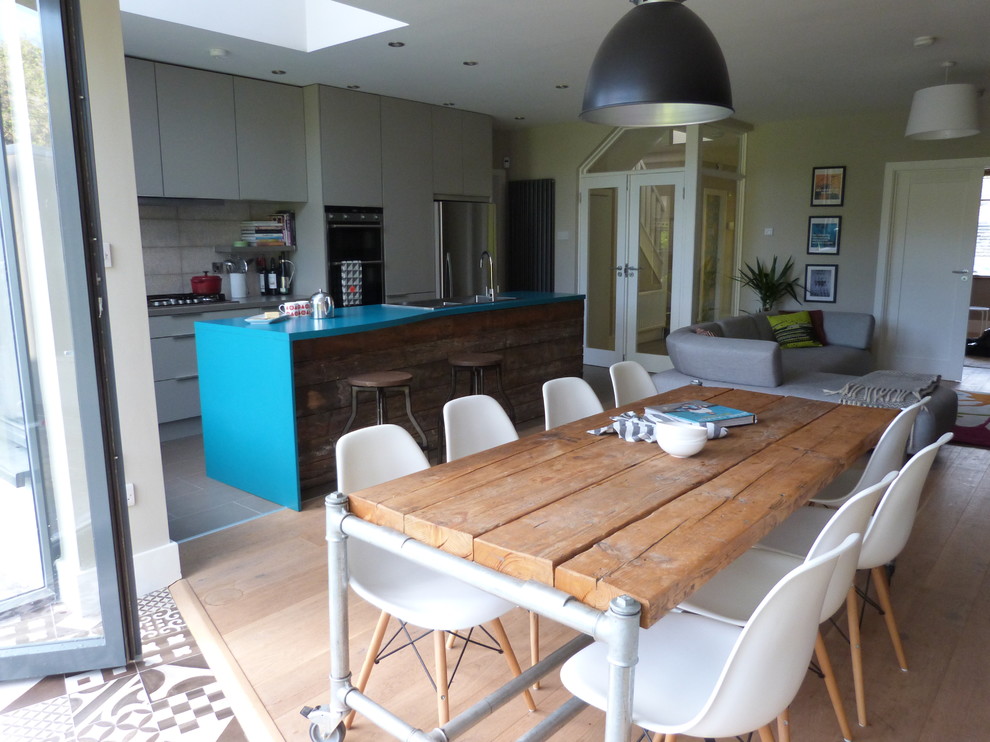 Photo of a mid-sized eclectic single-wall eat-in kitchen in Dublin with a double-bowl sink, flat-panel cabinets, grey cabinets, laminate benchtops, white splashback, porcelain splashback, stainless steel appliances, light hardwood floors and with island.