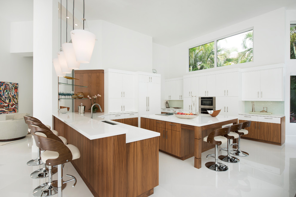 Example of a large transitional u-shaped porcelain tile and white floor kitchen design with an undermount sink, flat-panel cabinets, light wood cabinets, quartzite countertops, blue backsplash, glass tile backsplash, stainless steel appliances, an island and white countertops