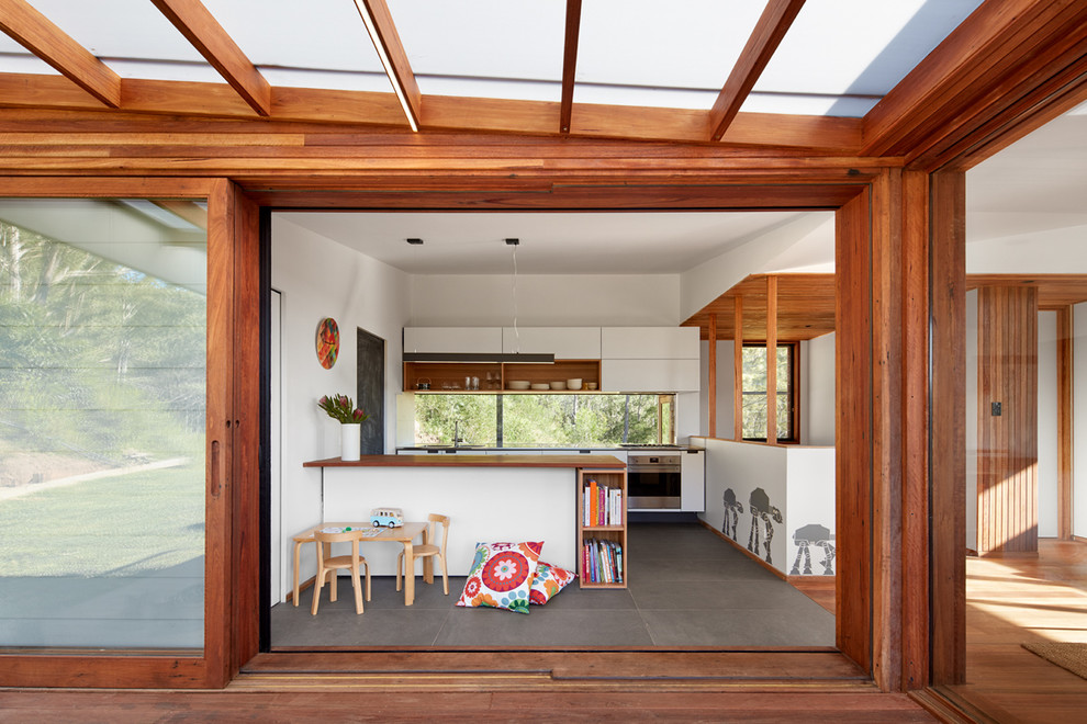 Design ideas for a midcentury kitchen in Wollongong with flat-panel cabinets, white cabinets, wood benchtops, window splashback, stainless steel appliances, concrete floors, a peninsula and grey floor.