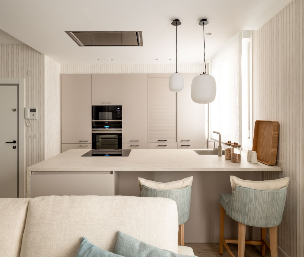 Design ideas for a small beach style galley open plan kitchen in Bilbao with an undermount sink, flat-panel cabinets, beige cabinets, quartz benchtops, black appliances, laminate floors, a peninsula and beige benchtop.