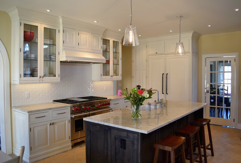 Photo of a transitional l-shaped open plan kitchen in Denver with a farmhouse sink, raised-panel cabinets, white cabinets, white splashback, subway tile splashback, stainless steel appliances and with island.