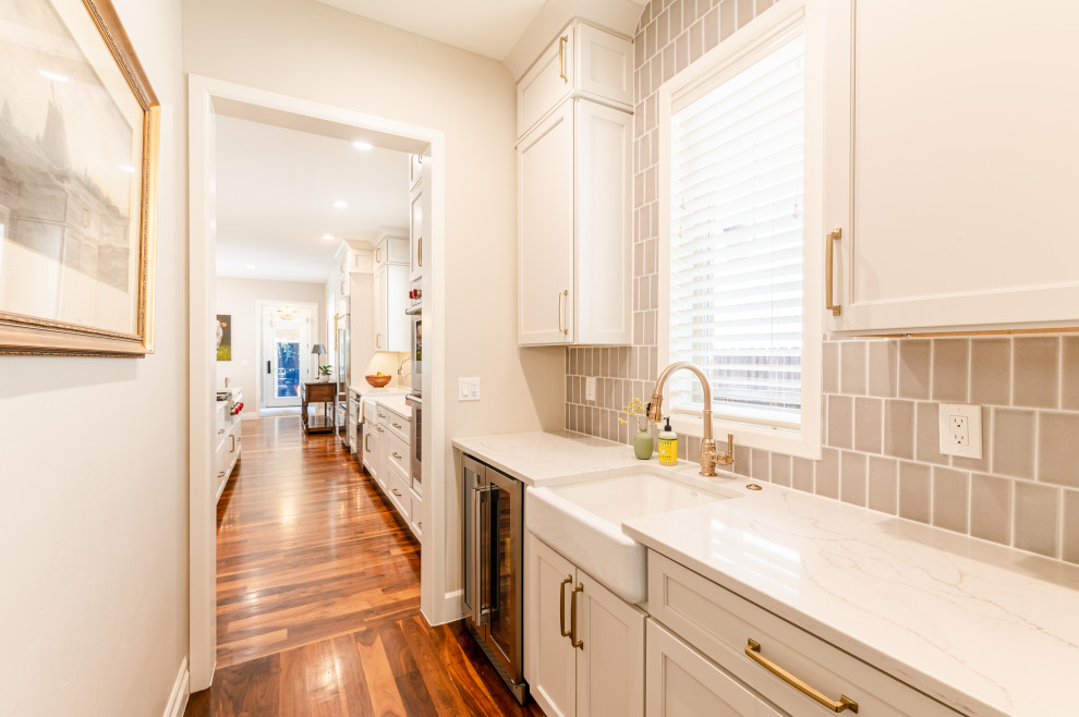 Inspiration for a large transitional l-shaped dark wood floor and brown floor open concept kitchen remodel in Denver with a farmhouse sink, shaker cabinets, beige cabinets, quartz countertops, beige backsplash, ceramic backsplash, stainless steel appliances, an island and white countertops