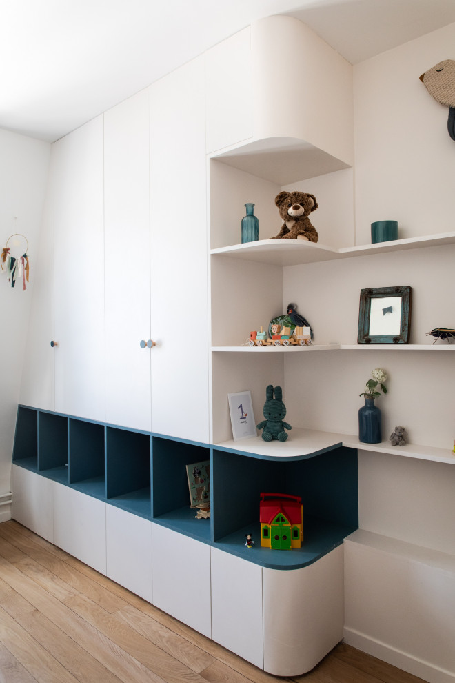 Immagine di una cameretta per neonati neutra minimal con pareti bianche, parquet chiaro e travi a vista