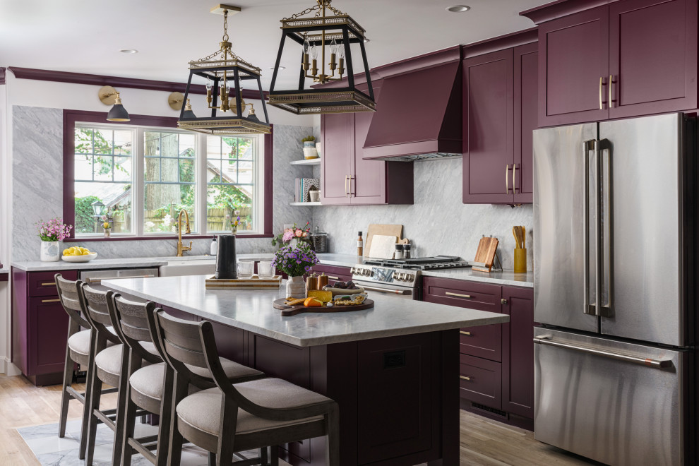 Photo of a transitional l-shaped eat-in kitchen in Kansas City with a farmhouse sink, recessed-panel cabinets, marble benchtops, marble splashback, stainless steel appliances, light hardwood floors, with island, purple cabinets, grey splashback, beige floor and grey benchtop.