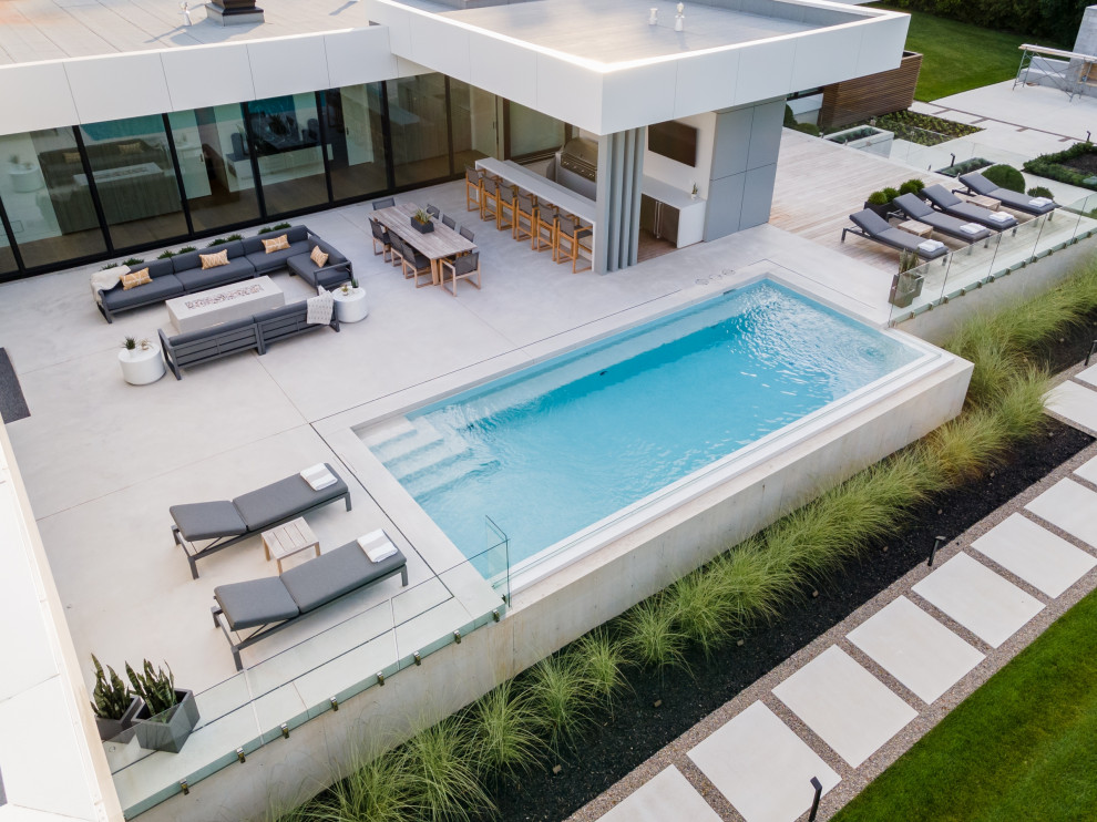 Esempio di una piccola piscina a sfioro infinito design rettangolare dietro casa con paesaggistica bordo piscina e lastre di cemento