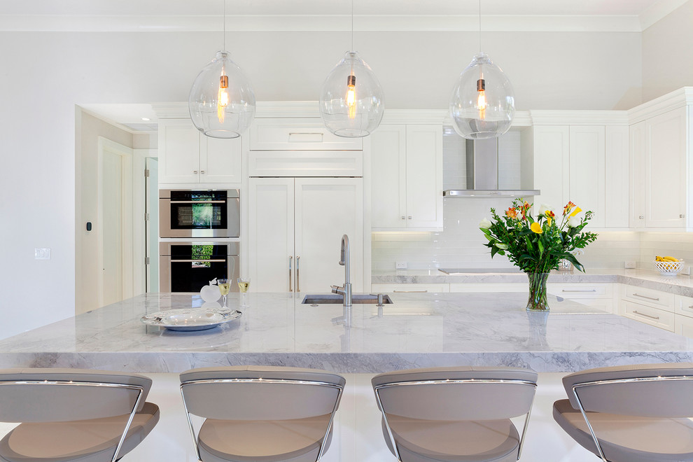 Large transitional galley enclosed kitchen photo in Miami with a drop-in sink, recessed-panel cabinets, white cabinets, marble countertops, white backsplash, ceramic backsplash, stainless steel appliances, an island and gray countertops