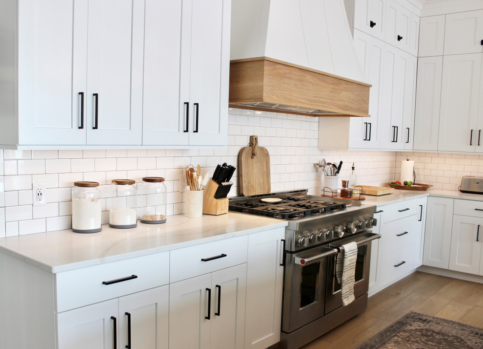 Foto på ett stort vintage vit kök, med en rustik diskho, släta luckor, vita skåp, bänkskiva i kvarts, vitt stänkskydd, stänkskydd i porslinskakel, rostfria vitvaror, ljust trägolv, en köksö och brunt golv