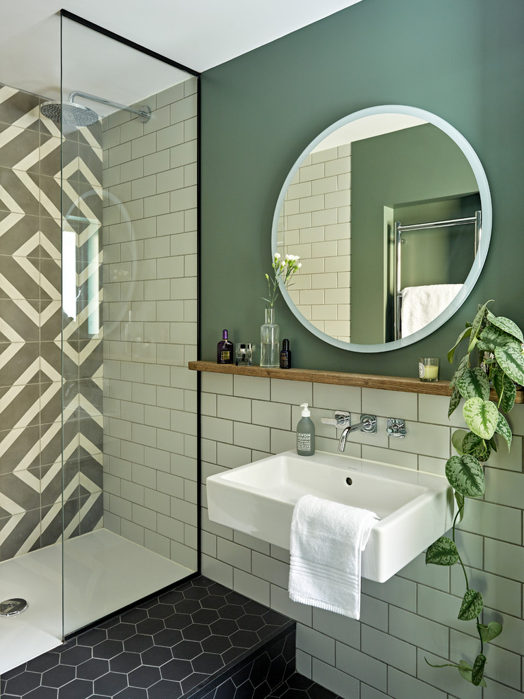 Design ideas for a mid-sized modern 3/4 bathroom in London with flat-panel cabinets, blue cabinets, an open shower, a wall-mount toilet, gray tile, cement tile, green walls, porcelain floors, a wall-mount sink, wood benchtops, black floor, an open shower and brown benchtops.