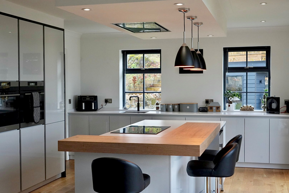 Large modern grey and black kitchen with grey cabinets, black appliances, an island and white worktops.