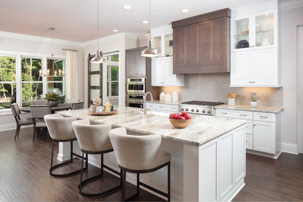 Large transitional galley brown floor kitchen photo with a farmhouse sink, shaker cabinets, white cabinets, gray backsplash, stainless steel appliances, an island and gray countertops