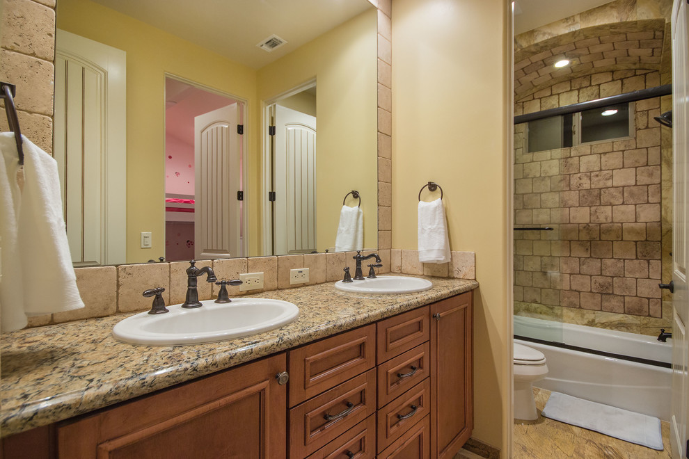 This is an example of a mid-sized mediterranean kids bathroom in Los Angeles with a drop-in sink, recessed-panel cabinets, medium wood cabinets, granite benchtops, an undermount tub, a corner shower, a two-piece toilet, beige tile, ceramic tile, beige walls and ceramic floors.