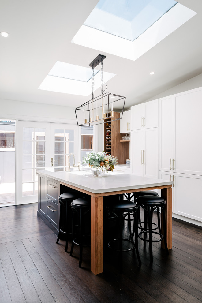 This is an example of a large transitional galley eat-in kitchen in Hobart with a farmhouse sink, shaker cabinets, white cabinets, quartz benchtops, yellow splashback, ceramic splashback, stainless steel appliances, dark hardwood floors, with island, brown floor and white benchtop.