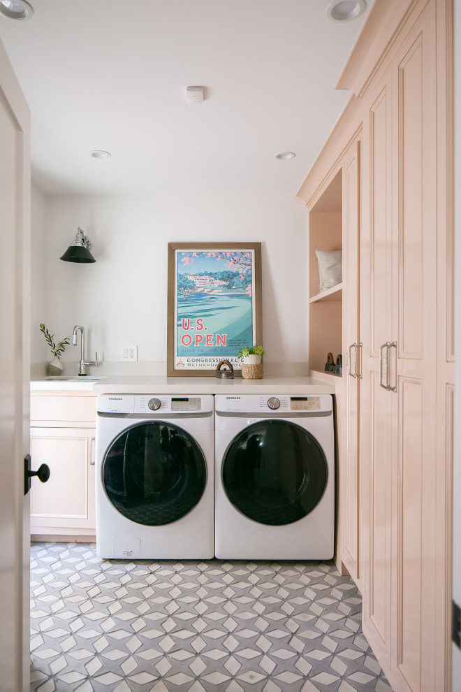 Exempel på en klassisk beige l-formad beige tvättstuga enbart för tvätt, med en undermonterad diskho, luckor med infälld panel, röda skåp, bänkskiva i kvarts, beige stänkskydd, vita väggar, en tvättmaskin och torktumlare bredvid varandra och flerfärgat golv