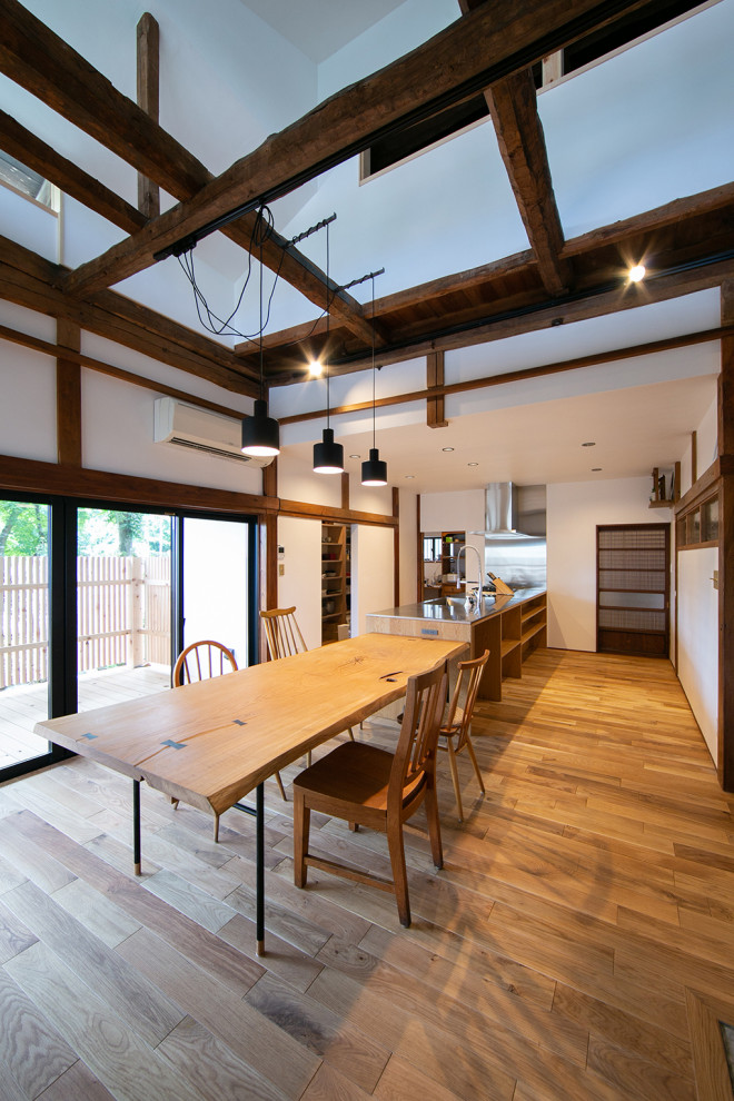 Mid-sized contemporary open plan dining in Other with white walls, medium hardwood floors, a wood stove, a concrete fireplace surround, beige floor and exposed beam.
