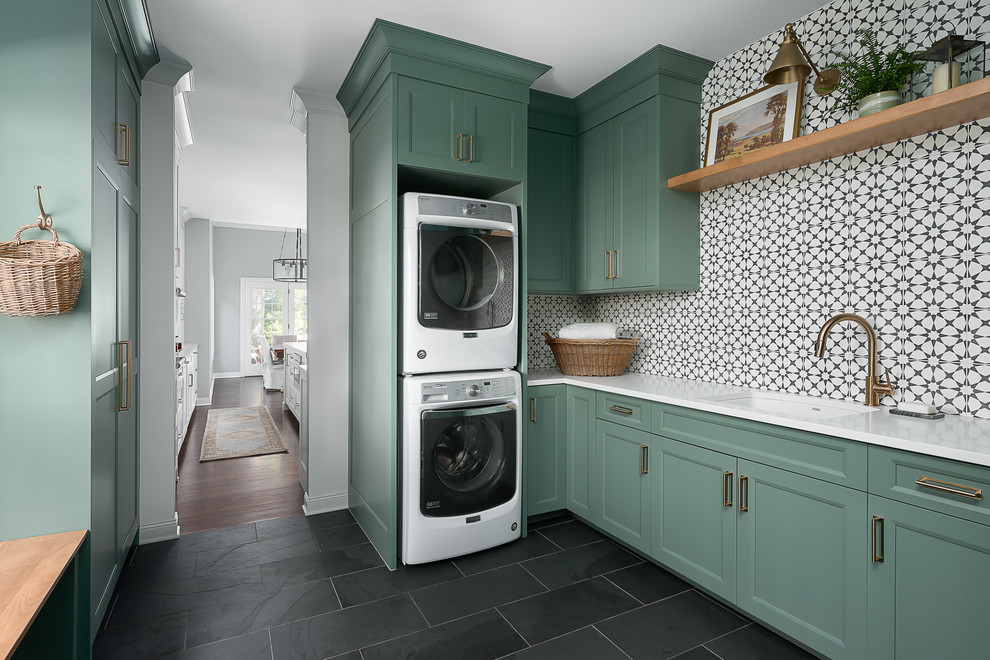 This is an example of a mid-sized transitional u-shaped utility room in Chicago with an undermount sink, shaker cabinets, green cabinets, quartz benchtops, white walls, porcelain floors, a stacked washer and dryer, black floor and white benchtop.