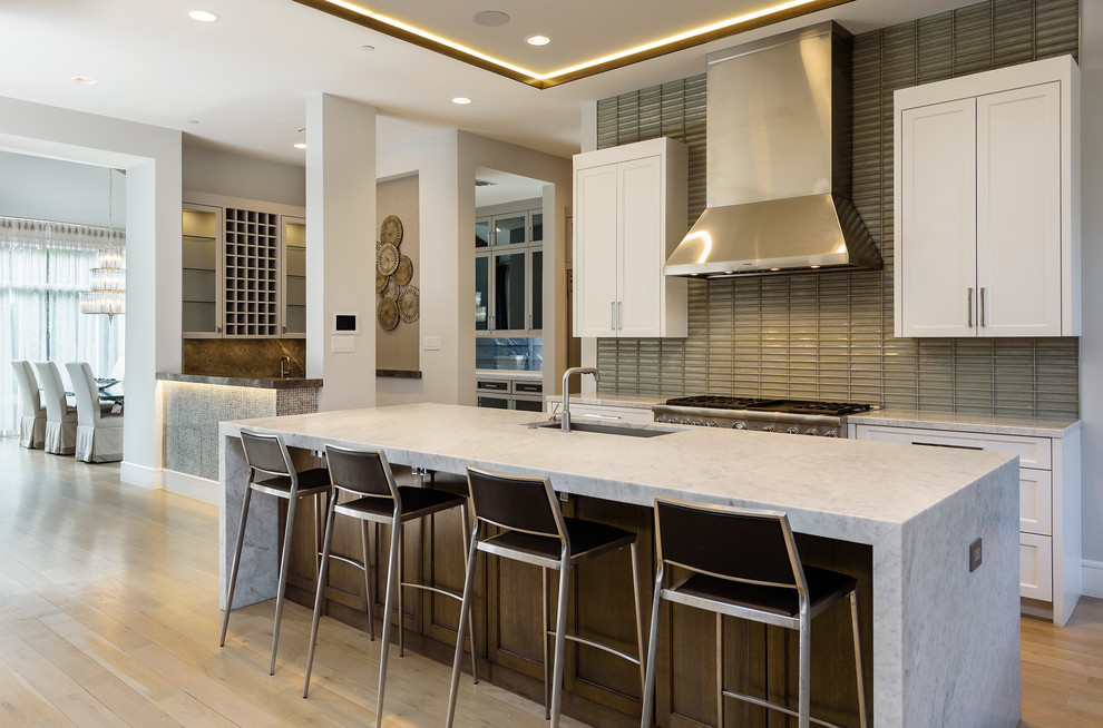 Example of a transitional galley light wood floor and beige floor open concept kitchen design in Dallas with an undermount sink, shaker cabinets, white cabinets, gray backsplash, glass tile backsplash, stainless steel appliances, an island and gray countertops