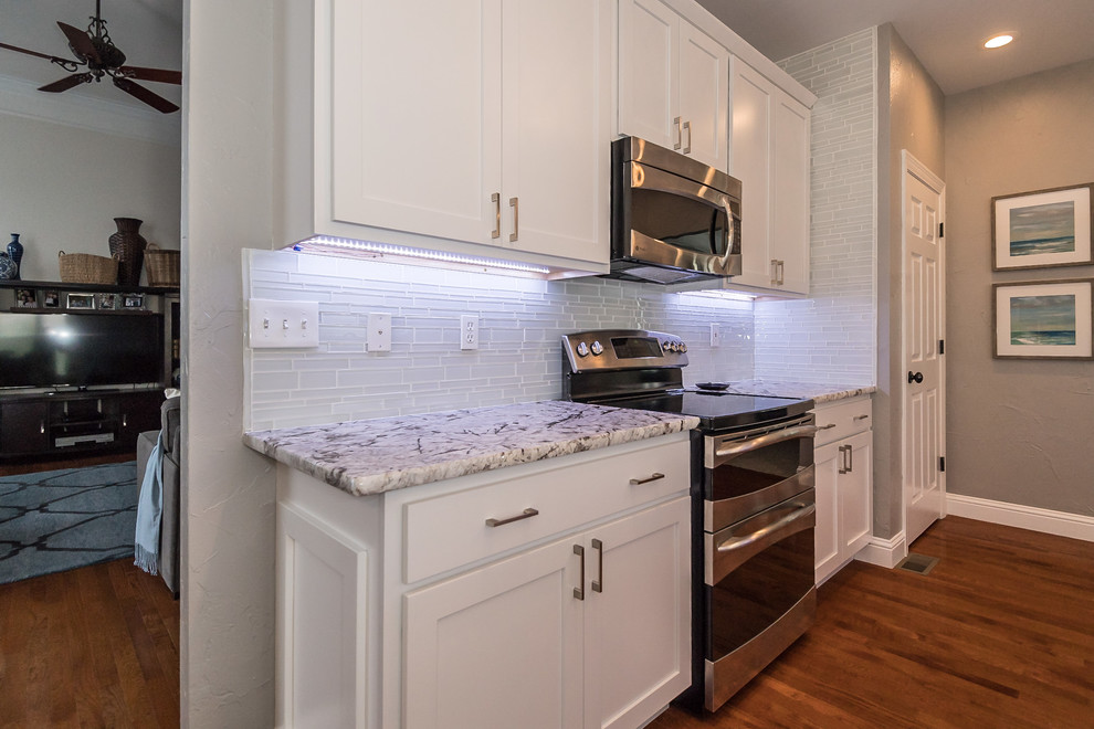 Mid-sized transitional u-shaped eat-in kitchen in St Louis with an undermount sink, shaker cabinets, white cabinets, granite benchtops, grey splashback, glass tile splashback, stainless steel appliances, dark hardwood floors, a peninsula and brown floor.