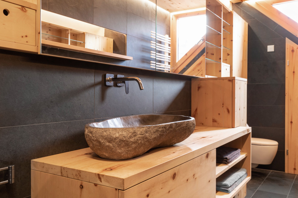 Photo of a small contemporary bathroom in Other with flat-panel cabinets, light wood cabinets, a curbless shower, a bidet, black tile, slate, black walls, slate floors, a trough sink, granite benchtops, black floor, an open shower, brown benchtops, an enclosed toilet, a single vanity, a floating vanity and wood.