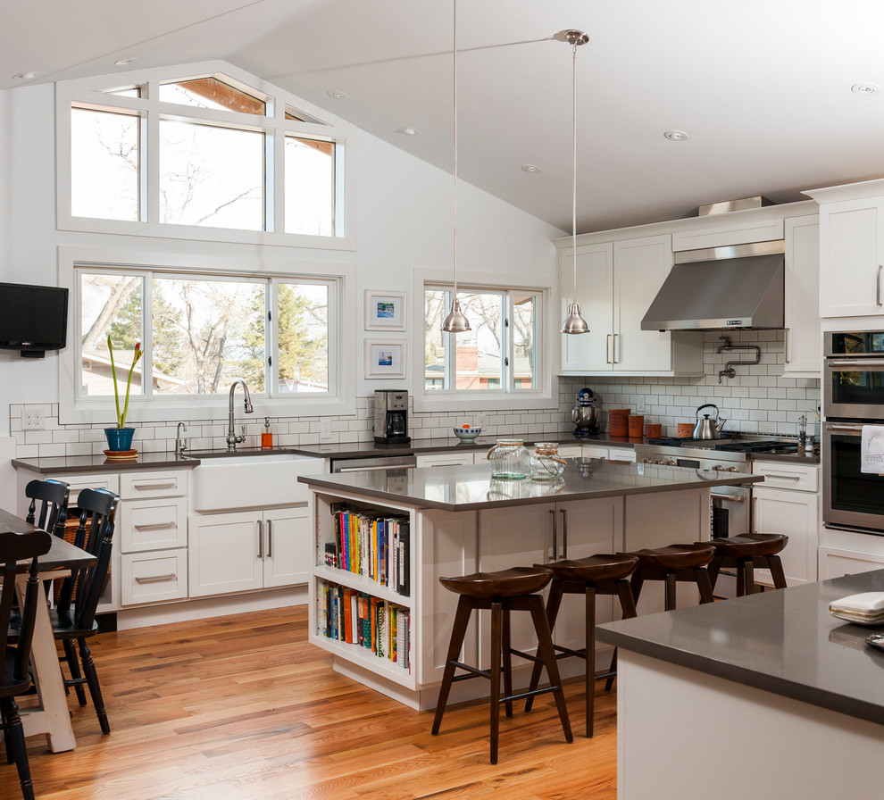 Design ideas for a large transitional u-shaped eat-in kitchen in Denver with a farmhouse sink, shaker cabinets, quartz benchtops, white splashback, subway tile splashback, stainless steel appliances, medium hardwood floors, with island, white cabinets and brown floor.
