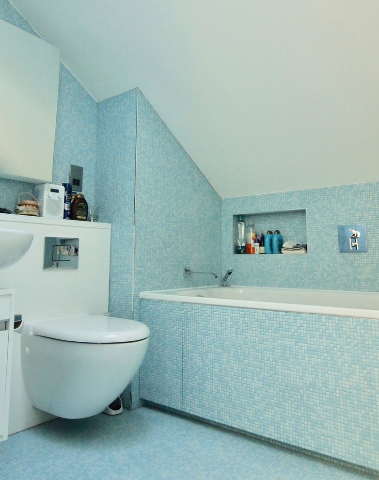 Mid-sized contemporary master bathroom in London with flat-panel cabinets, white cabinets, an alcove tub, a wall-mount toilet, blue tile, mosaic tile, solid surface benchtops, a hinged shower door, white benchtops, an alcove shower, blue walls, mosaic tile floors, a wall-mount sink and blue floor.