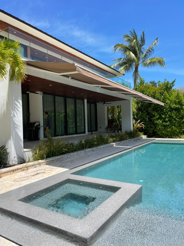 Inspiration for a large modern backyard patio in Miami with concrete pavers and an awning.