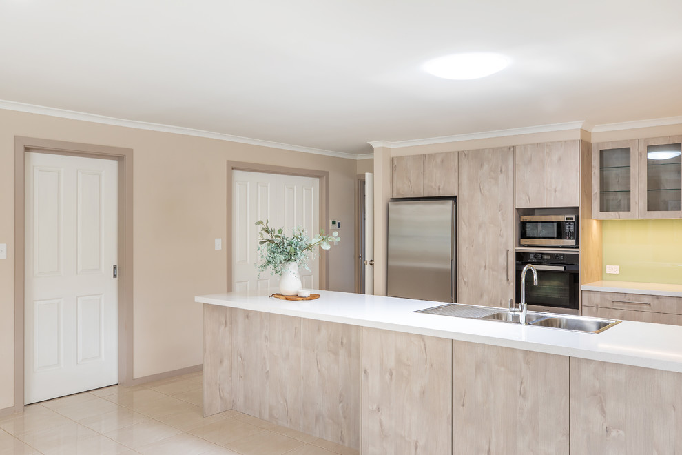 Inspiration for a mid-sized modern u-shaped kitchen pantry in Adelaide with a double-bowl sink, flat-panel cabinets, light wood cabinets, quartz benchtops, green splashback, glass sheet splashback, stainless steel appliances, porcelain floors, a peninsula, white floor and white benchtop.