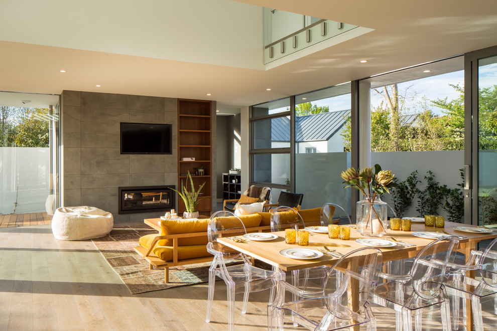 Photo of a large contemporary open plan dining in Christchurch with white walls, light hardwood floors, a ribbon fireplace, a tile fireplace surround and beige floor.