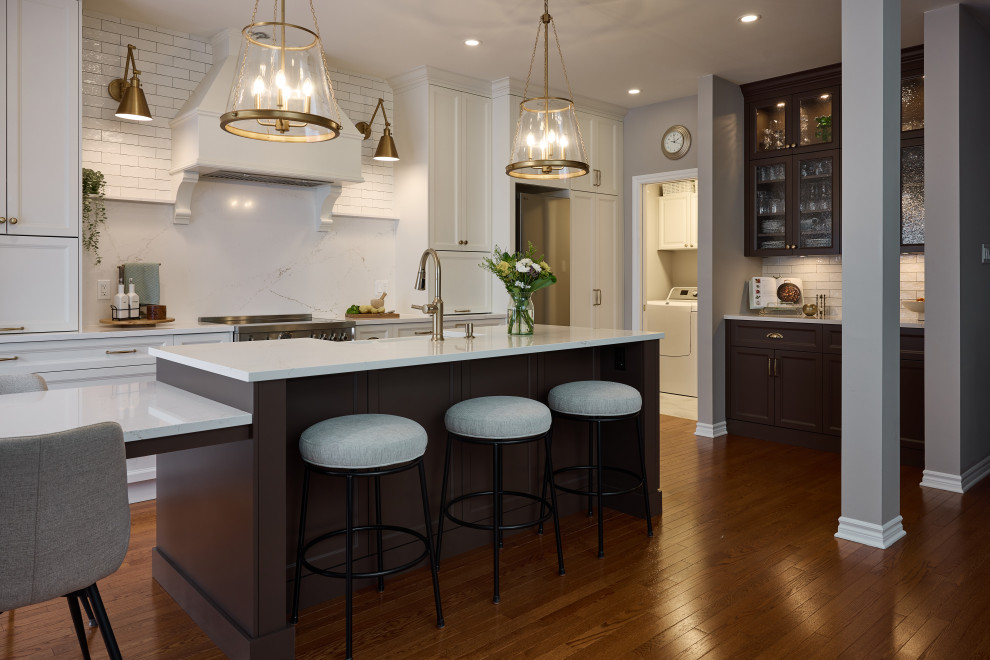 Example of a large transitional single-wall brown floor and medium tone wood floor eat-in kitchen design in Ottawa with white backsplash, stainless steel appliances, an island, white countertops, a farmhouse sink, quartz countertops, quartz backsplash, shaker cabinets and brown cabinets