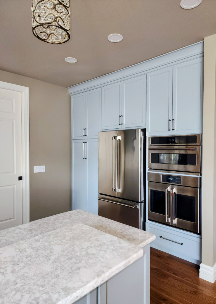 Open concept kitchen - mid-sized transitional medium tone wood floor and brown floor open concept kitchen idea with an undermount sink, shaker cabinets, quartz countertops, white backsplash, quartz backsplash, stainless steel appliances, an island and white countertops