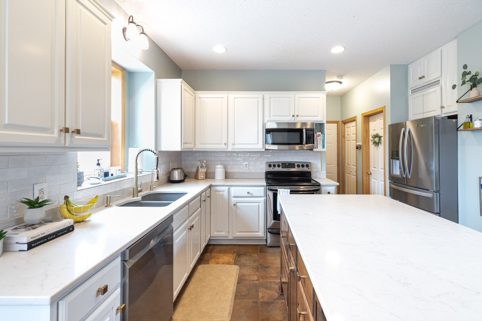 Photo of a mid-sized transitional l-shaped open plan kitchen in Minneapolis with an undermount sink, raised-panel cabinets, white cabinets, quartz benchtops, white splashback, ceramic splashback, stainless steel appliances, terra-cotta floors, with island, brown floor and white benchtop.