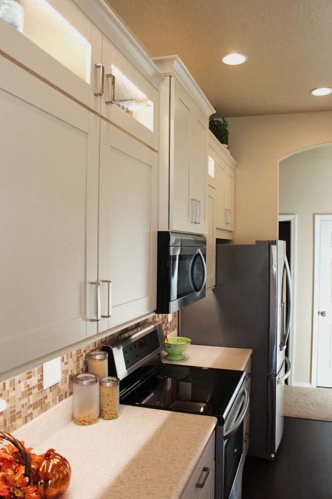 Transitional galley eat-in kitchen photo in Boise with an integrated sink, shaker cabinets, white cabinets, solid surface countertops, beige backsplash, glass tile backsplash and stainless steel appliances