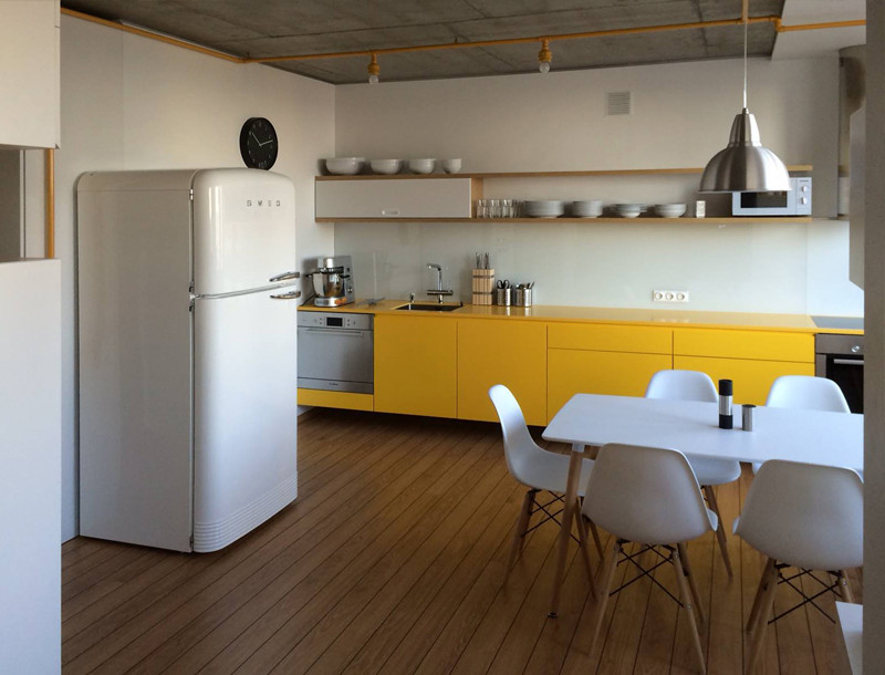 На фото: прямая кухня-гостиная среднего размера в стиле модернизм с плоскими фасадами, желтыми фасадами, бежевым фартуком, полом из ламината, островом и желтой столешницей