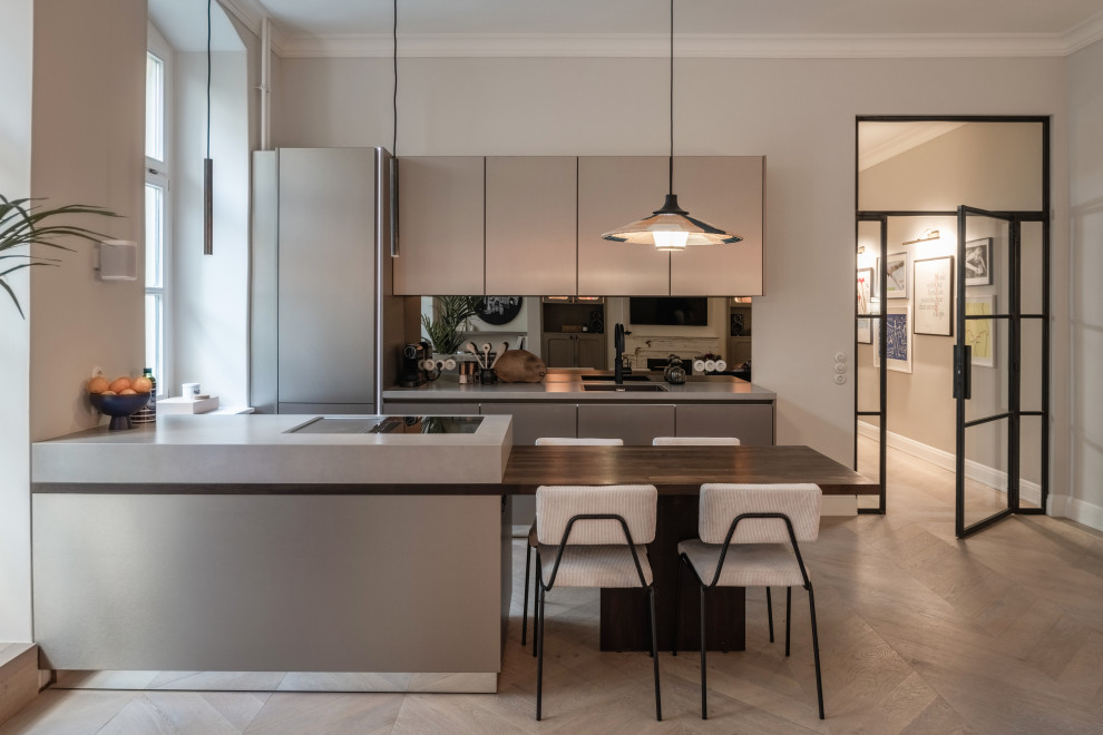 Design ideas for a mid-sized contemporary galley kitchen in Berlin with an undermount sink, flat-panel cabinets, grey cabinets, metallic splashback, mirror splashback, panelled appliances, medium hardwood floors, a peninsula, brown floor and grey benchtop.