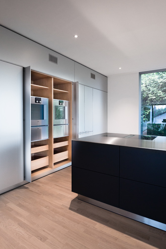 Design ideas for an expansive contemporary open plan kitchen in Other with a double-bowl sink, flat-panel cabinets, stainless steel cabinets, stainless steel benchtops, brown splashback, stainless steel appliances, light hardwood floors and with island.