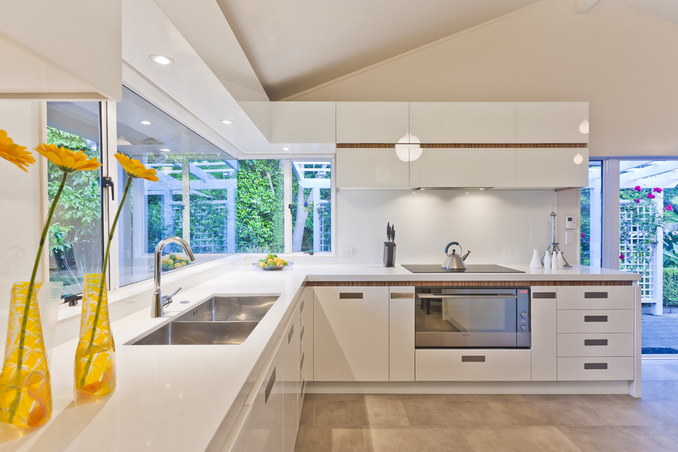 Contemporary u-shaped open plan kitchen in Los Angeles with a double-bowl sink, flat-panel cabinets, white cabinets, solid surface benchtops, white splashback, glass sheet splashback, stainless steel appliances, a peninsula and white floor.