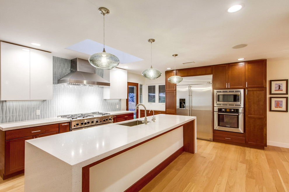 Inspiration for a large midcentury l-shaped separate kitchen with a single-bowl sink, recessed-panel cabinets, medium wood cabinets, quartz benchtops, blue splashback, glass tile splashback, stainless steel appliances, light hardwood floors, with island, beige floor and white benchtop.