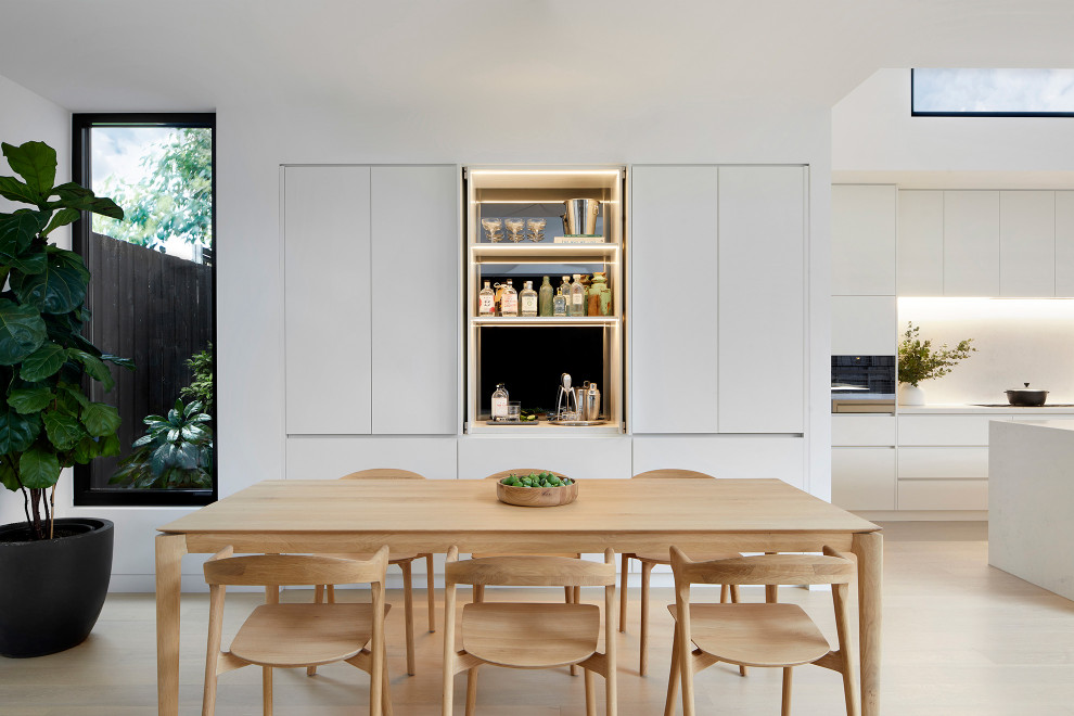 This is an example of a modern open plan dining in Melbourne with white walls, light hardwood floors and beige floor.