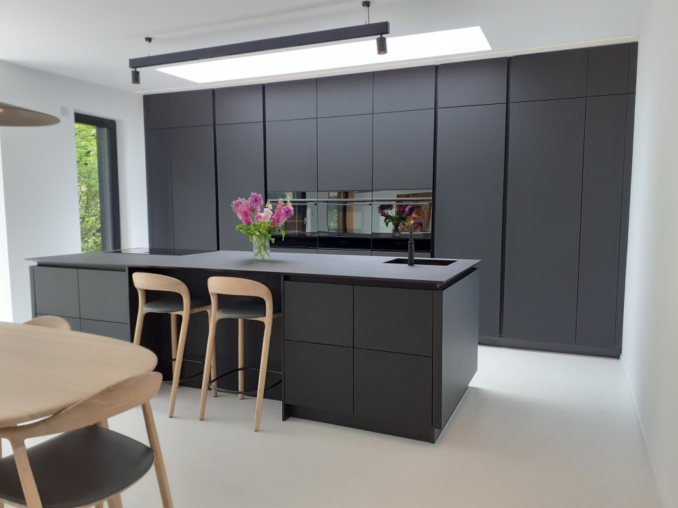 Offene, Mittelgroße Moderne grifflose Küche mit flächenbündigen Schrankfronten, schwarzen Schränken, schwarzen Elektrogeräten, Kücheninsel und schwarzer Arbeitsplatte in Buckinghamshire