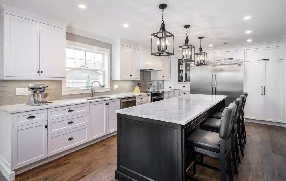 Kitchen - large transitional l-shaped medium tone wood floor and brown floor kitchen idea with an undermount sink, white cabinets, quartz countertops, white backsplash, glass tile backsplash, stainless steel appliances, an island and white countertops