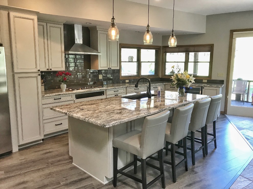 Large transitional l-shaped eat-in kitchen in Phoenix with a farmhouse sink, white cabinets, granite benchtops, brown splashback, subway tile splashback, stainless steel appliances, porcelain floors, with island, grey floor, beige benchtop and recessed-panel cabinets.
