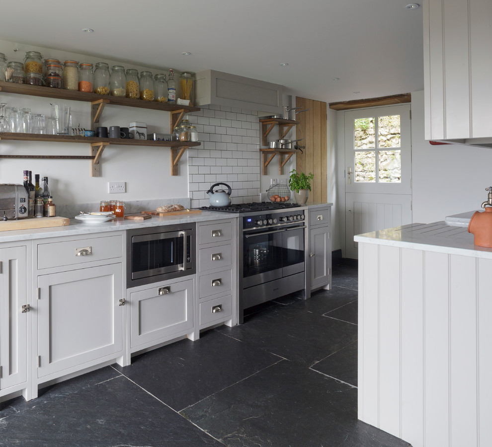 Small country kitchen in Cornwall with shaker cabinets, grey cabinets, no island, marble benchtops, white splashback, subway tile splashback, stainless steel appliances and black floor.