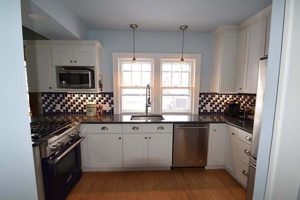 Example of a small transitional l-shaped light wood floor kitchen design with an undermount sink, shaker cabinets, white cabinets, quartz countertops, multicolored backsplash, ceramic backsplash, stainless steel appliances and a peninsula