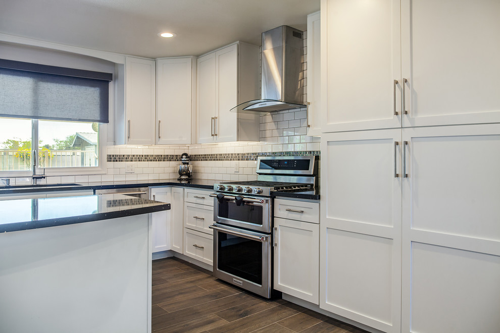 Inspiration for a large transitional l-shaped porcelain tile and brown floor eat-in kitchen remodel in Phoenix with an undermount sink, recessed-panel cabinets, white cabinets, quartz countertops, black backsplash, ceramic backsplash, stainless steel appliances and an island