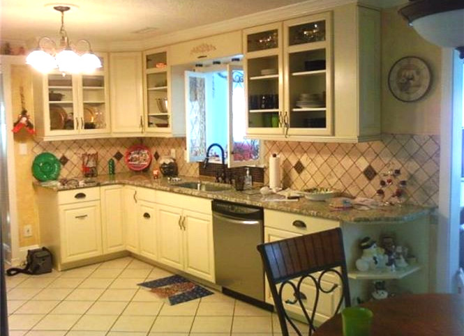 Mid-sized elegant l-shaped ceramic tile eat-in kitchen photo in Charlotte with a drop-in sink, raised-panel cabinets, white cabinets, granite countertops, beige backsplash, stone tile backsplash, stainless steel appliances and no island