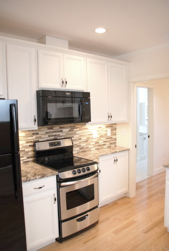 Photo of a small transitional l-shaped open plan kitchen in Detroit with an undermount sink, recessed-panel cabinets, white cabinets, quartz benchtops, multi-coloured splashback, glass tile splashback, black appliances and medium hardwood floors.