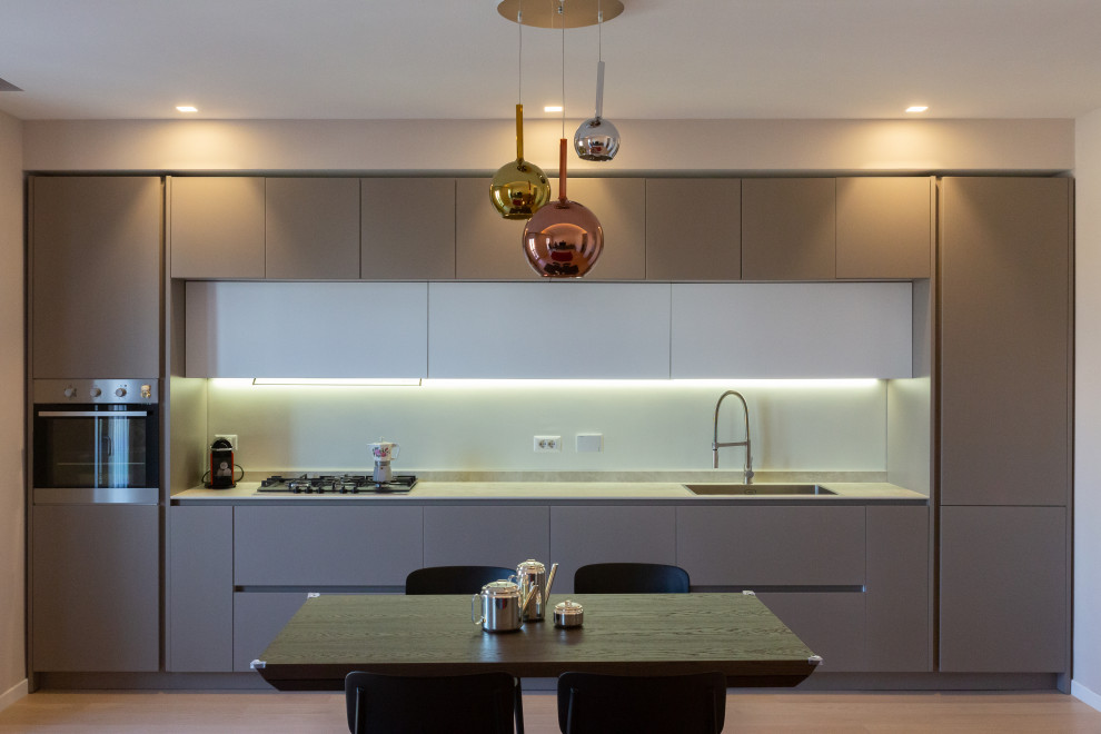 Small modern single-wall eat-in kitchen in Rome with an undermount sink, flat-panel cabinets, beige cabinets, solid surface benchtops, beige splashback, stainless steel appliances, light hardwood floors, beige benchtop and recessed.