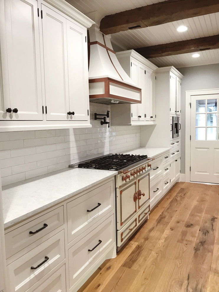 Exempel på ett stort lantligt vit vitt kök, med en rustik diskho, luckor med infälld panel, vita skåp, bänkskiva i kvarts, vitt stänkskydd, stänkskydd i tunnelbanekakel, integrerade vitvaror, mellanmörkt trägolv, en köksö och flerfärgat golv